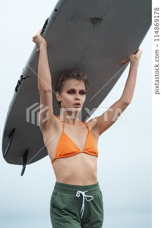 Closeup of female surfer carrying white surfboard on her head during summer vacation. Sensuality female athlete wearing bikini top and shorts. Image is representation of concepts of sports activities 114869178