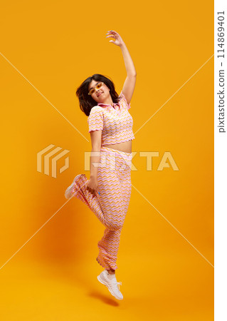Youth culture. Young Indian woman in fashion outfit dancing of joy against vibrant yellow studio background. Youth culture. Young Indian woman in fashion outfit dancing of joy against vibrant yellow studio background. 114869401