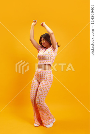 Party mood. Full length portrait of young Indian woman dancing of joy and happiness against vibrant yellow studio background. 114869405