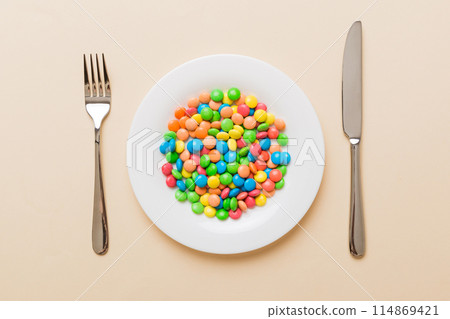 cutlery on table and sweet plate of candy. Health and obesity concept, top view on colored background cutlery on table and sweet plate of candy. Health and obesity concept, top view on colored background 114869421