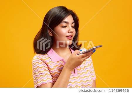 Portrait of you Indian girl talking on smartphone against vibrant yellow studio background. Customer. Ordering. Portrait of you Indian girl talking on smartphone against vibrant yellow studio background. Customer. Ordering. 114869456