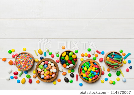 different colored round candy in bowl and jars. Top view of large variety sweets and candies with copy space different colored round candy in bowl and jars. Top view of large variety sweets and candies with copy space 114870007