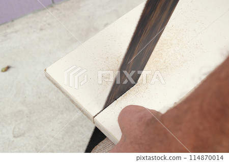 Man cutting through wooden board with hand saw in garden Man cutting through wooden board with hand saw in garden 114870014