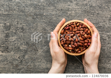 Woman hands holding a wooden bowl with peanuts. Healthy food and snack. Vegetarian snacks of different nuts Woman hands holding a wooden bowl with peanuts. Healthy food and snack. Vegetarian snacks of different nuts 114870036