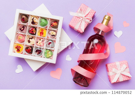 Bottle of red wine on colored background for Valentine Day with gift and chocolate. Heart shaped with gift box of chocolates top view with copy space 114870052