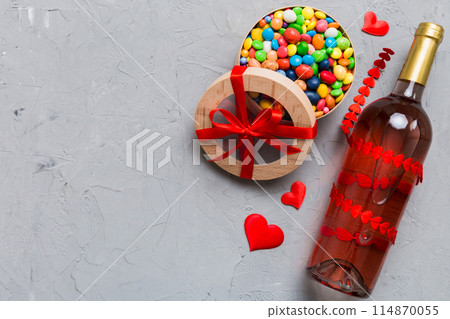 Bottle of red wine on colored background for Valentine Day with gift and chocolate. Heart shaped with gift box of chocolates top view with copy space 114870055