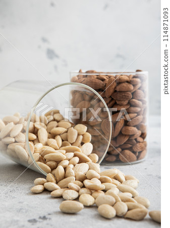 Glass jars with healthy raw almond whole and peeled nuts on white kitchen table. 114871093