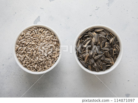Whole and peeled healthy sunflower seeds in ceramic bowl plates on light kitchen table. Whole and peeled healthy sunflower seeds in ceramic bowl plates on light kitchen table. 114871097