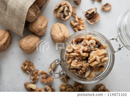 Peeled walnut nuts in glass jar and linen bag with whole nuts on light background. 114871102