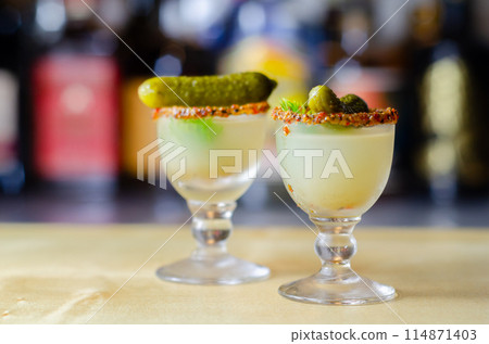 Shaken vodka and pickle juice with ice in a shot glass and garnished with small pickled cucumber and dill 114871403