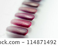 A row of purple patterns of painted nail plates are arranged on a white surface 114871492