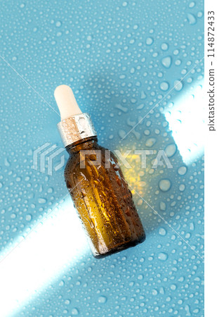 Serum bottle , oil cosmetic on blue background with hard light and water drops. with shadows flat lay, top view Serum bottle , oil cosmetic on blue background with hard light and water drops. with shadows flat lay, top view 114872433