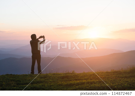 Man Taking Photo of Sunset on Mountain Peak 114872467