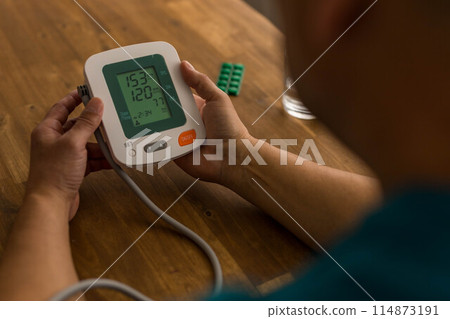 Seniory man checks blood pressure with monitor on upper arm in room  114873191