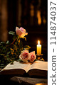 Two pink roses placed on an open bible beside a lit candle 114874037