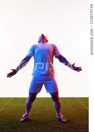 Champion. Football player with arms wide open leaned back freezing in moment of triumph in neon light against white studio background. Champion. Football player with arms wide open leaned back freezing in moment of triumph in neon light against white studio background. 114874739