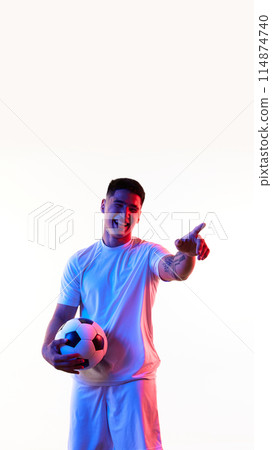 Poster. Young man, football athlete posing with ball and pointing to distance in neon light against white studio background. 114874740