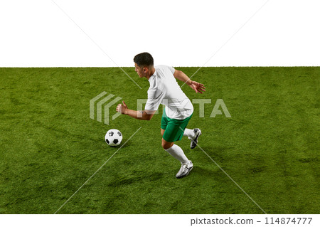 Dynamic image of athlete in green shorts and white shirt, running to strike soccer ball with force, caught mid-motion on field. Dynamic image of athlete in green shorts and white shirt, running to strike soccer ball with force, caught mid-motion on field. 114874777