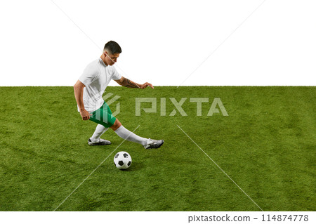 Young athletic man, soccer player in prepares to kicking ball on green grass field against white studio background. 114874778