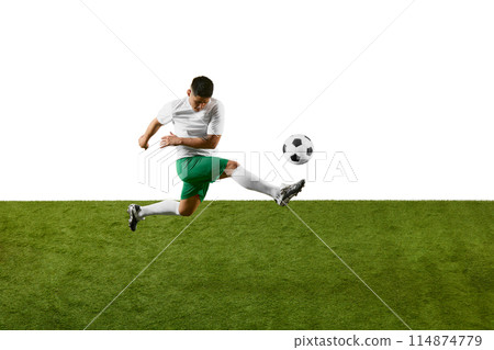 Dynamic photo of young athlete man, soccer player training to kicking ball in motion on green field against white studio background. 114874779