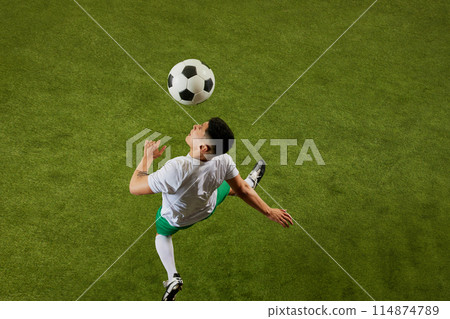 Aerial view of soccer player intensely focused on black and white football player which flying above him. 114874789