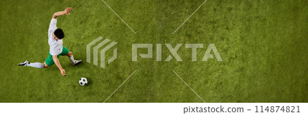 Banner. Aerial view of young man, soccer player in green shorts and white jersey striking soccer ball on lush green field. 114874821