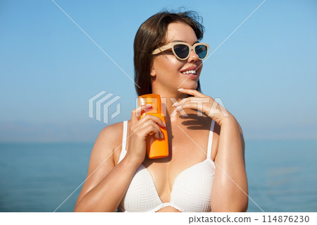 Beautiful woman applying cream sunscreen on tanned face. Sunscreen. Skin and body care. The girl uses a sunscreen for her skin. Portrait of a female holding suntan lotion and moisturizing sunscreen. Beautiful woman applying cream sunscreen on tanned face. Sunscreen. Skin and body care. The girl uses a sunscreen for her skin. Portrait of a female holding suntan lotion and moisturizing sunscreen. 114876230