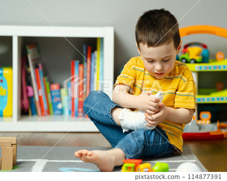 A little toddler boy holds his leg in a cast with his hands. Fracture of a foot and finger in children. Human healthcare and medicine concept. Bandage A little toddler boy holds his leg in a cast with his hands. Fracture of a foot and finger in children. Human healthcare and medicine concept. Bandage 114877391