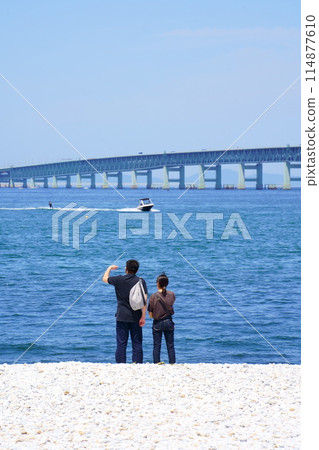A man and a woman looking at the Kansai Airport Link Bridge from Marble Beach in Rinku Park (Izumisano City, Osaka Prefecture) 114877610