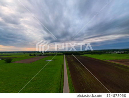 A road winds through fields under a dramatic sky, creating a picturesque scene of rural beauty 114878068