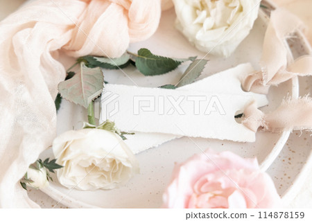 Cards near light pink fabric and cream flowers on plate close up, copy space, wedding mockup Cards near light pink fabric and cream flowers on plate close up, copy space, wedding mockup 114878159