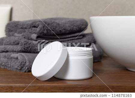 White cosmetic jar near grey folded towels and basin on wooden countertop in bath, mockup White cosmetic jar near grey folded towels and basin on wooden countertop in bath, mockup 114878163