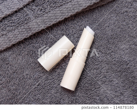 Opened lip balm stick on grey towels near basin and green monstera in bath, lid mockup 114878180