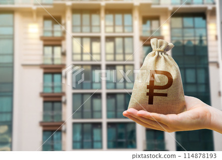 Russian ruble bag against the background of modern high-rise buildings. Investing in the purchase of real estate. Affordable housing and mortgage rates. Renting apartments and houses. Blurred 114878193