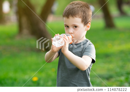 Three year old caucasian toddler boy drinks water from a bottle in the park on a spring or summer day. 114878222