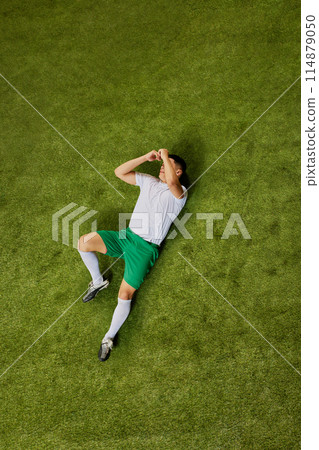 Bird's eye view of footballer on ground, covering his face with both hands, expressing emotions of exhaustion. 114879050