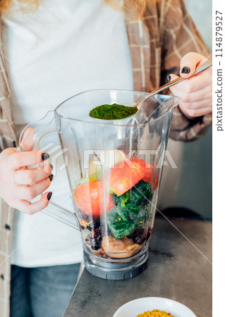 Close up woman adding spirulina or chlorella powder during making smoothie on the kitchen. Superfood supplement. Healthy detox vegan diet. Healthy dieting eating, weight loss program. Selective focus Close up woman adding spirulina or chlorella powder during making smoothie on the kitchen. Superfood supplement. Healthy detox vegan diet. Healthy dieting eating, weight loss program. Selective focus 114879527
