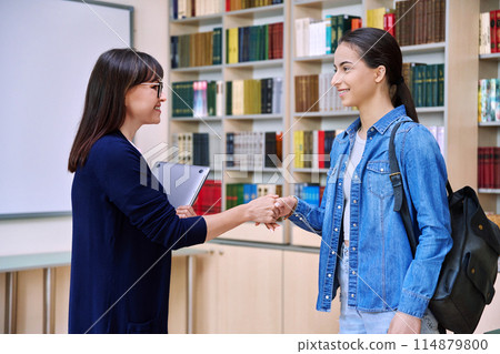 Female teacher shaking hands to teenage girl high school student, inside educational building Female teacher shaking hands to teenage girl high school student, inside educational building 114879800