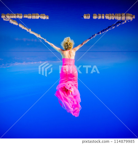 Elegant woman in pink dress suspended in surreal blue sky Elegant woman in pink dress suspended in surreal blue sky 114879985