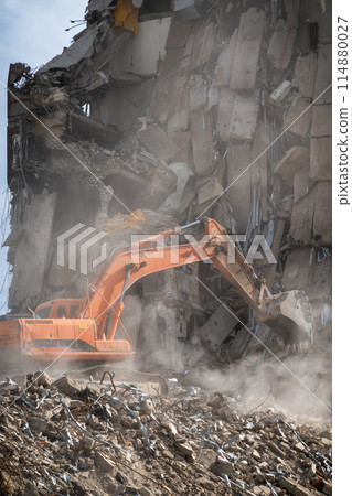 Excavator demolishing a large building with debris and dust Excavator demolishing a large building with debris and dust 114880027