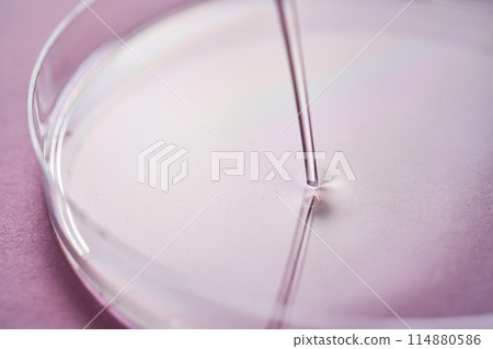 Serum or cosmetic oil flows into a transparent bowl on a purple background. 114880586
