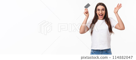 Waist-up of enthusiastic, happy surprised young woman reacting to wonderful news, raising hands up in amazement, holding credit card, receive salary, got her first paycheck, hurry to order something 114882047