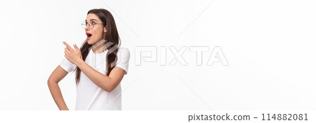 Waist-up portrait of amused and surprised young excited brunette girl 20s, wear glasses and casual t-shirt, turn head looking and pointing at upper left corner with dropped jaw from amazement Waist-up portrait of amused and surprised young excited brunette girl 20s, wear glasses and casual t-shirt, turn head looking and pointing at upper left corner with dropped jaw from amazement 114882081