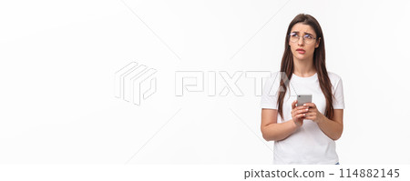 Communication, technology and lifestyle concept. Portrait of troubled and concerned young woman worried for friend, sending text message if shes okay and thinking, look up nervous, hold mobile phone 114882145