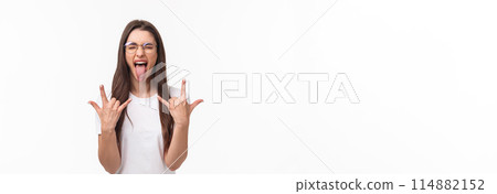 Rock-n-roll baby. Portrait of enthusiastic good-looking young girl having fun on awesome concert, show tongue close eyes and dancing with heavy metal sign, stand white background Rock-n-roll baby. Portrait of enthusiastic good-looking young girl having fun on awesome concert, show tongue close eyes and dancing with heavy metal sign, stand white background 114882152