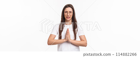 Waist-up portrait of desperate, hopeful young cute girl, sobbing and crying while praying, begging for mercy, ask something from person, feeling distressed, standing white background 114882266