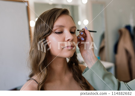 Backstage of the photo shoot: Make-up artist applies makeup on beautiful white model. Backstage of the photo shoot: Make-up artist applies makeup on beautiful white model. 114882682