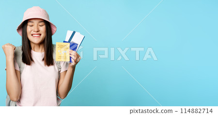 Happy asian girl triumphing, showing vaccination certificate, health passport and flight tickets, celebrating about trip, tourist feeling joy, standing over blue background Happy asian girl triumphing, showing vaccination certificate, health passport and flight tickets, celebrating about trip, tourist feeling joy, standing over blue background 114882714