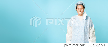 Portrait of smiling asian female doctor or nurse, wearing personal protective equipment and looking happy, standing over blue background Portrait of smiling asian female doctor or nurse, wearing personal protective equipment and looking happy, standing over blue background 114882721