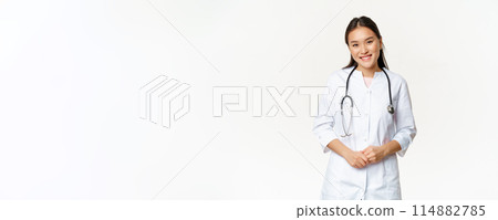 Smiling asian woman doctor, wearing medical robe and stethoscope, looking pleasant at patient, standing over white background Smiling asian woman doctor, wearing medical robe and stethoscope, looking pleasant at patient, standing over white background 114882785